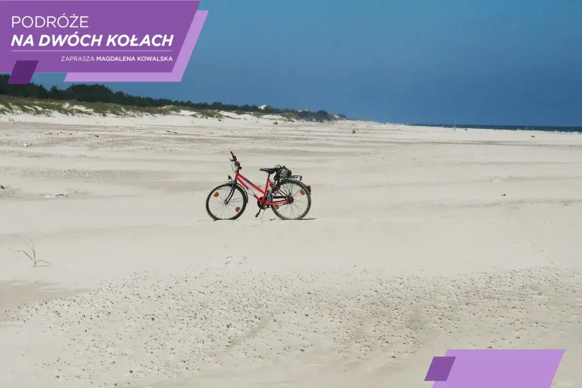 Czerwony rower na piaszczystej plaży, zapraszający do odkrywania szlak zwiniętych torów.