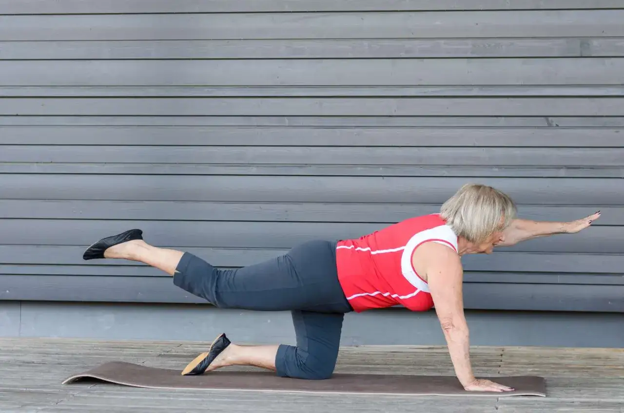 Donna di 50 anni in posizione di quadrupedia, solleva una gamba e un braccio. Esercizio di ginnastica per dimagrire a 50 anni.