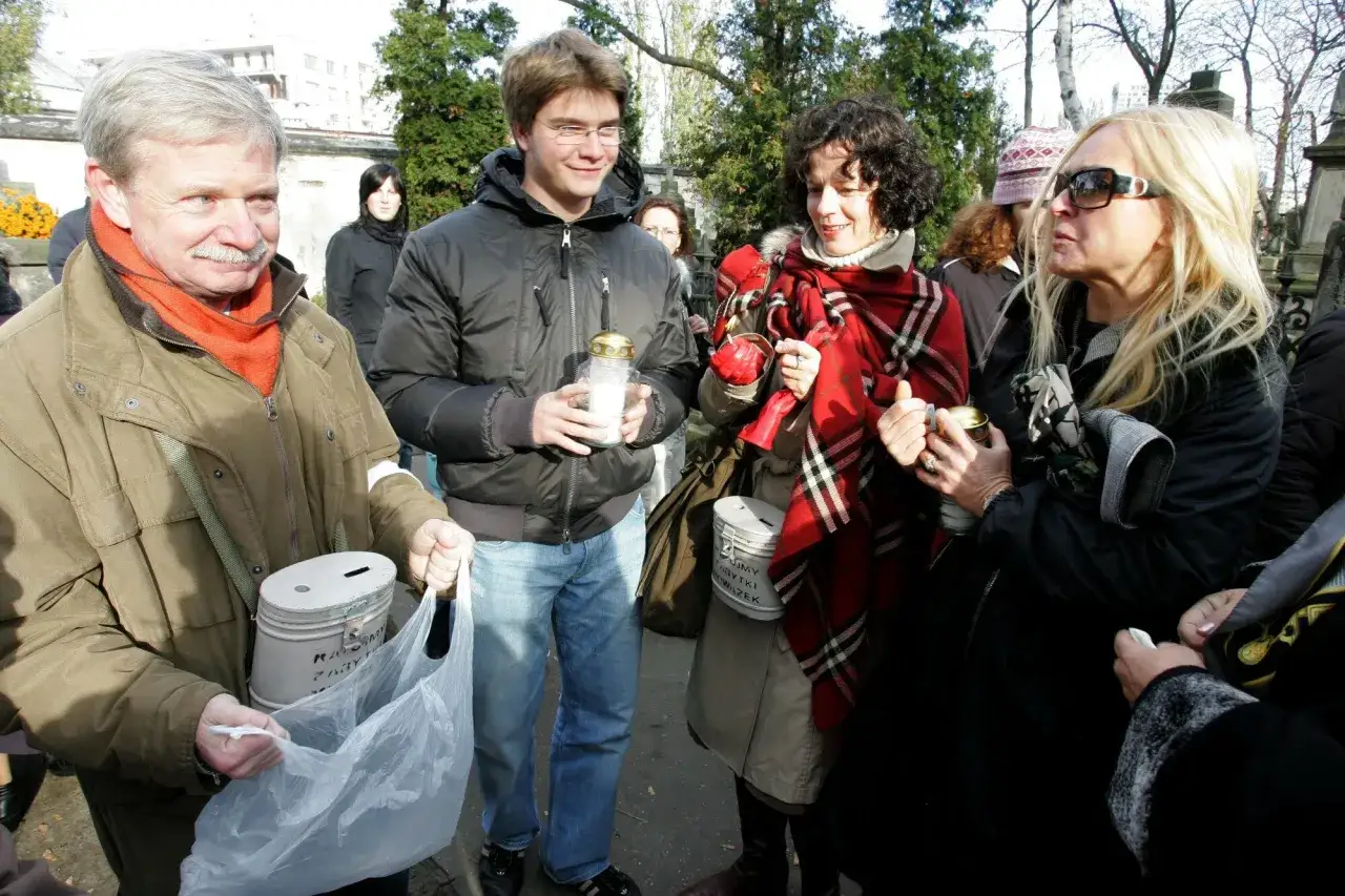 Grzegorz Wąsowski i Monika Olejnik na cmentarzu, trzymają znicze i puszki na datki.
