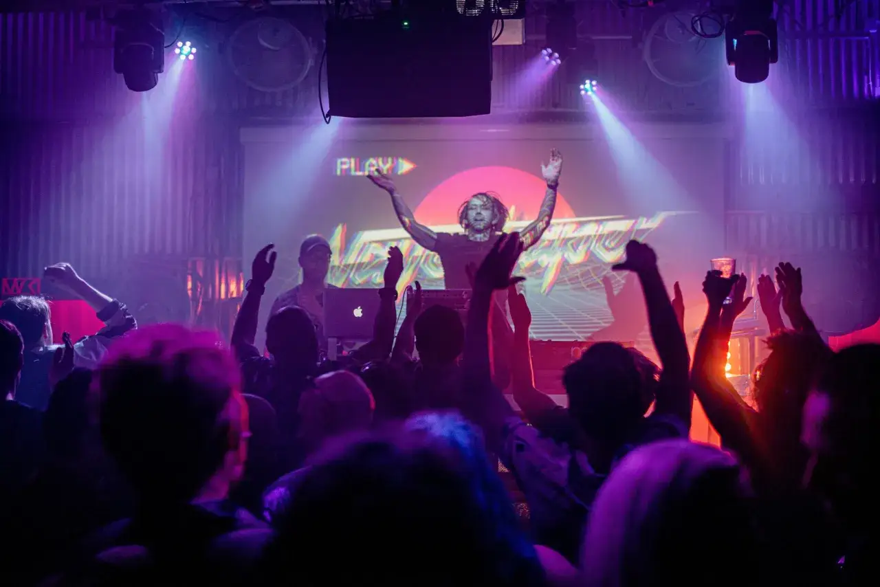 Publik jublar på en konsert i slaktkyrkan Stockholm. En DJ med armarna uppe framför en stor skärm.