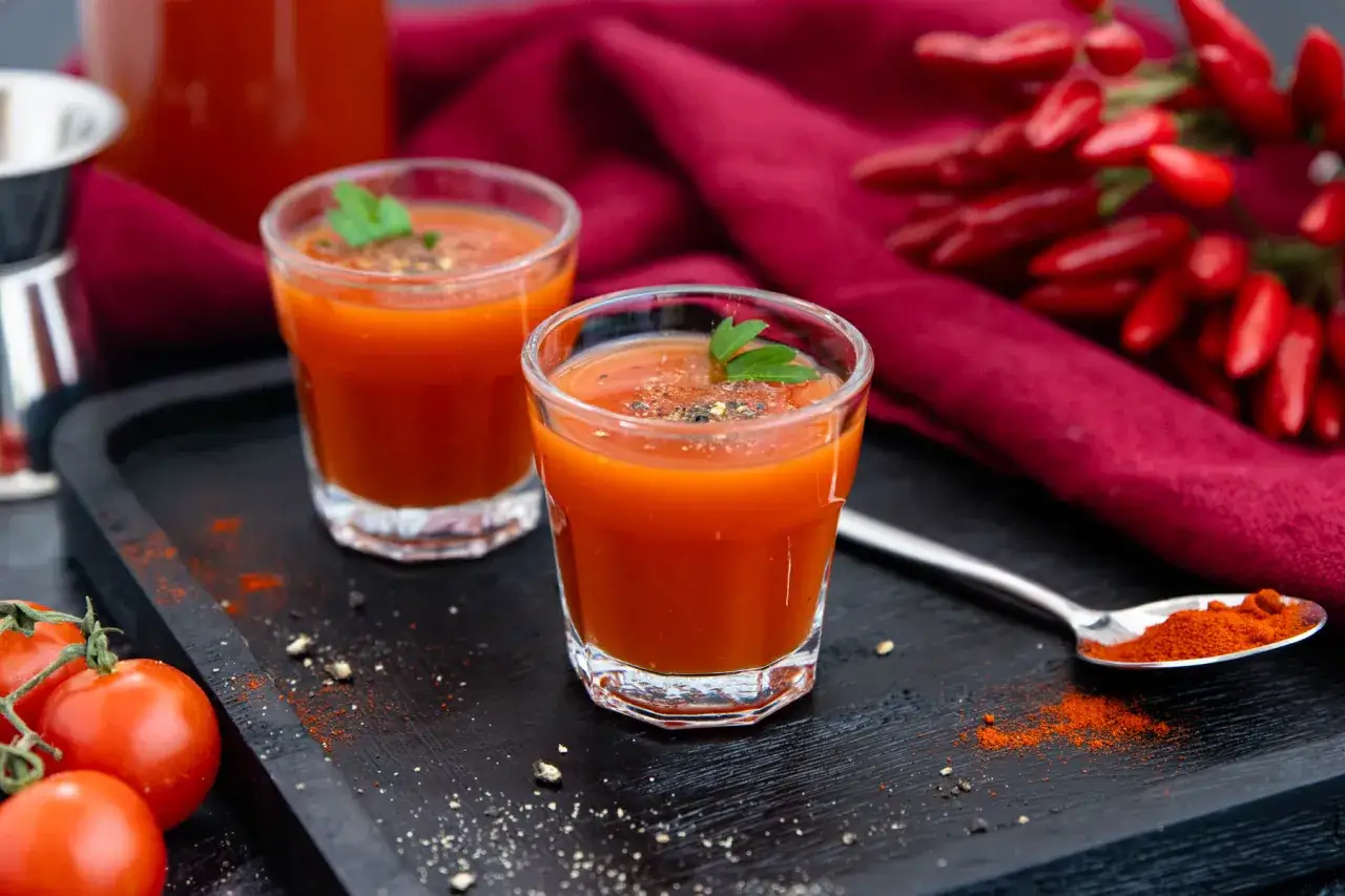 Zwei Gläser scharfer Tomatensaft, perfekt für ein mexikaner rezept. Frische Tomaten und Chilis im Hintergrund.