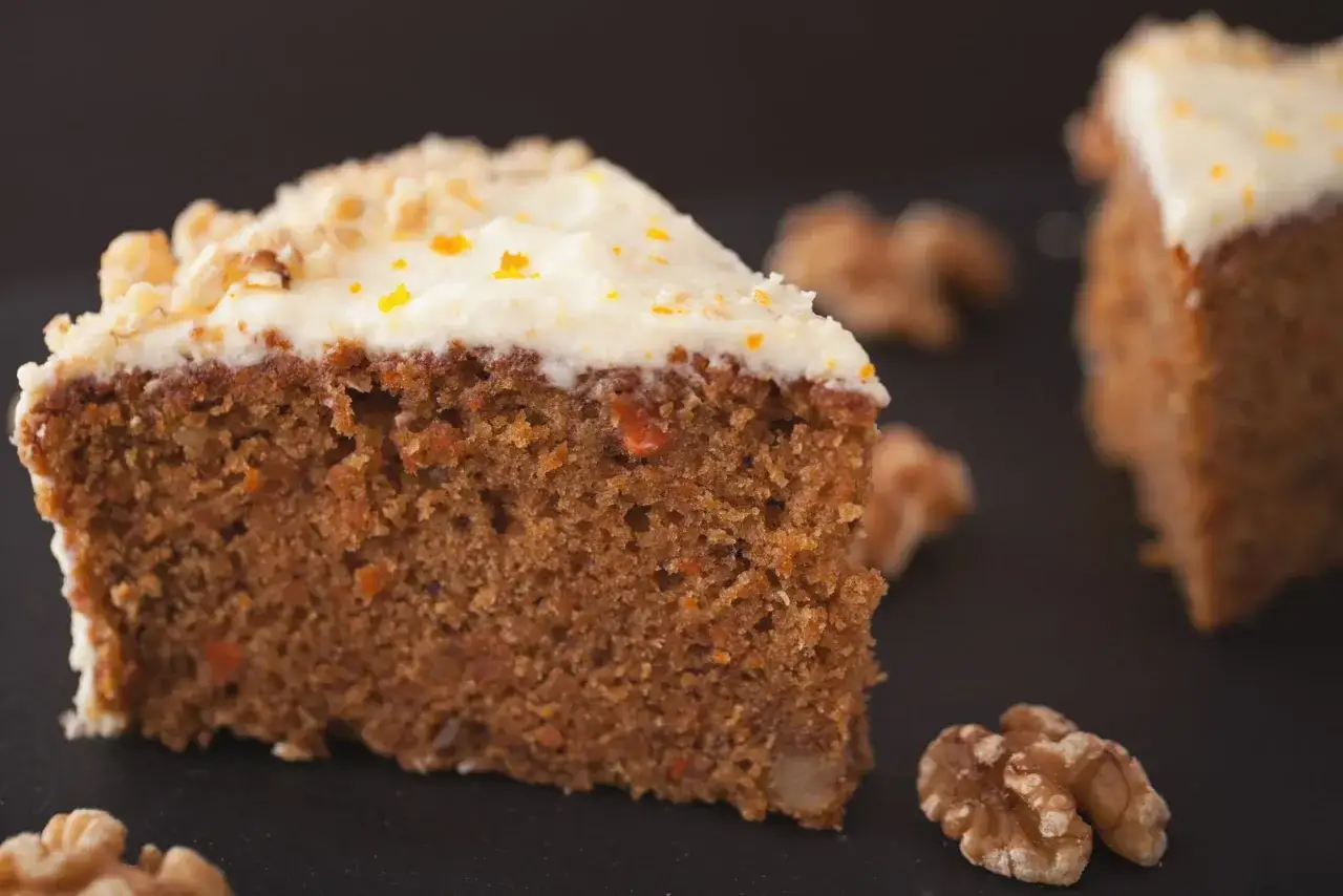 Fetta di torta di carote con glassa bianca e noci, un'opzione deliziosa per chi cerca dolci senza zucchero.