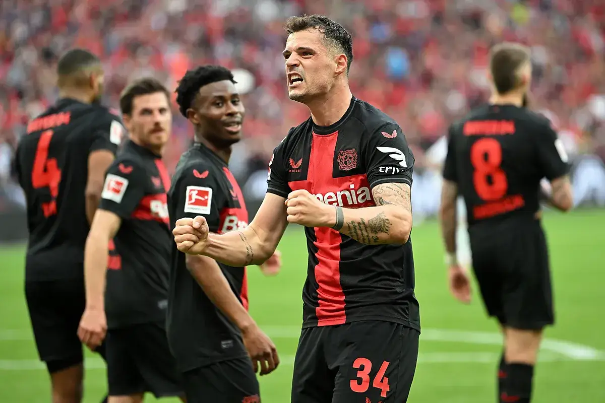 Piłkarze Bayer 04 Leverkusen świętują zwycięstwo. Jeden z nich, z numerem 34, unosi pięści w geście triumfu.