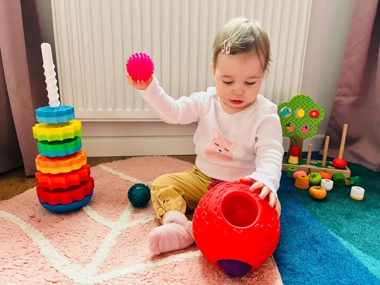 Roczne dziecko bawi się kolorowymi zabawkami: kulkami, wieżą i sorterem.