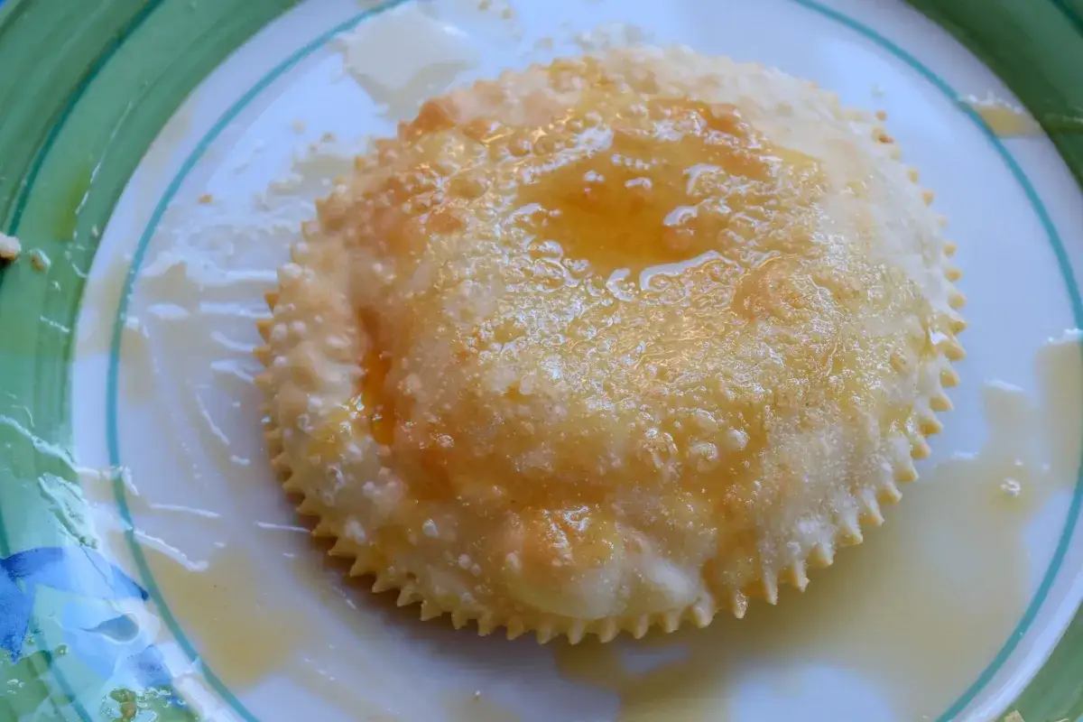 Un dolce sardo dorato e croccante, cosparso di miele dorato, su un piatto bianco con bordo verde.
