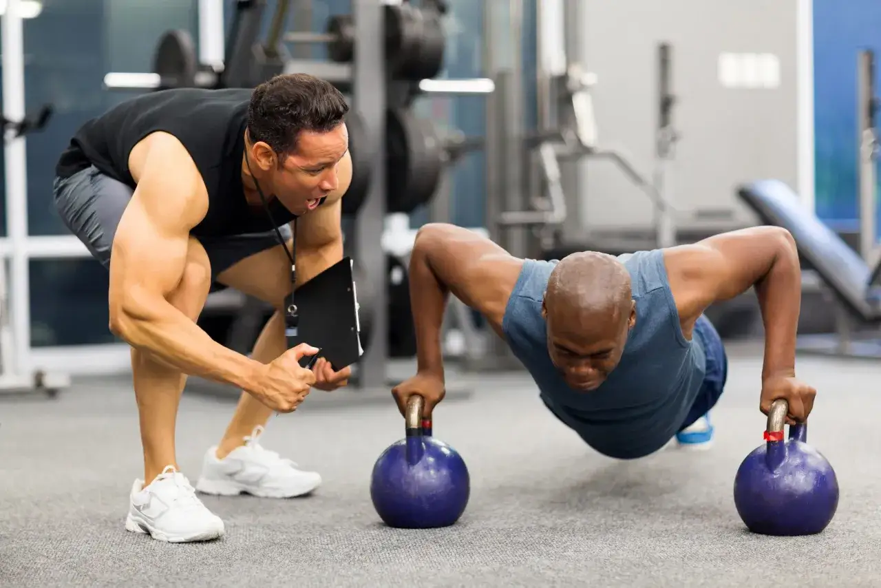 Un coach encourage un homme &agrave; faire des pompes avec des kettlebells. La motivation sport est palpable dans cette s&eacute;ance d'entra&icirc;nement intense.