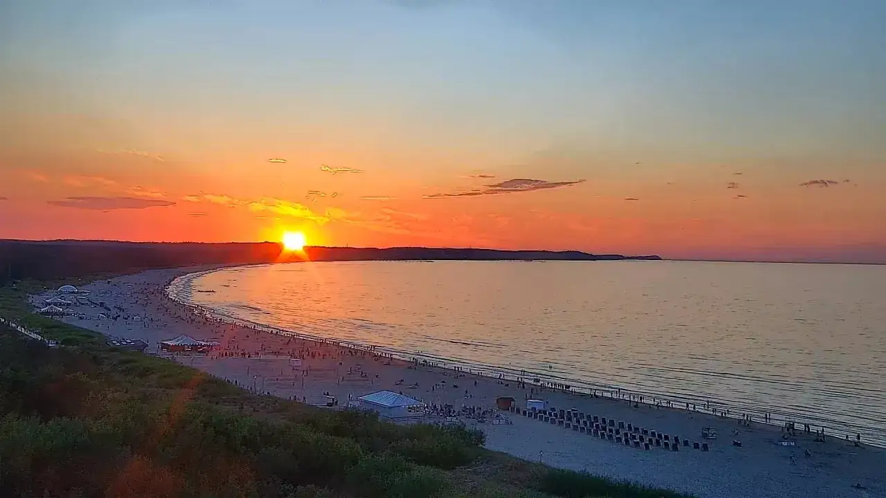 Zachód słońca w Świnoujściu nad Bałtykiem. Tłumy ludzi na plaży podziwiają pomarańczowe niebo i spokojne morze.