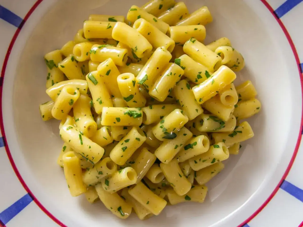 Pyszna pasta jajeczna z twarogiem, posypana świeżą natką pietruszki, w białej misce z kolorowym brzegiem.