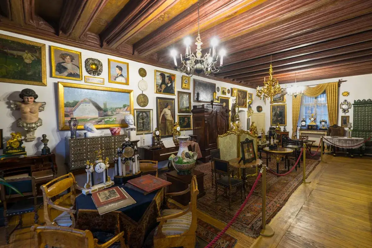Wnętrze pełne antyków i obrazów, przypominające salon z dawnych lat. To jedno z wielu fascynujących muzeów w Krakowie.