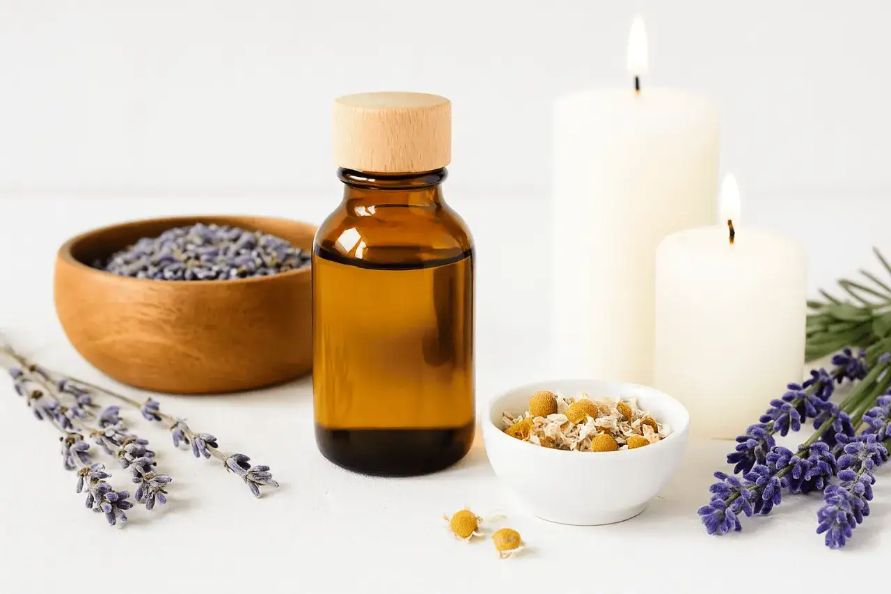 Eine Flasche ätherisches Öl, Lavendel und Kamille für Aromatherapie Anwendung. Zwei Kerzen brennen sanft.