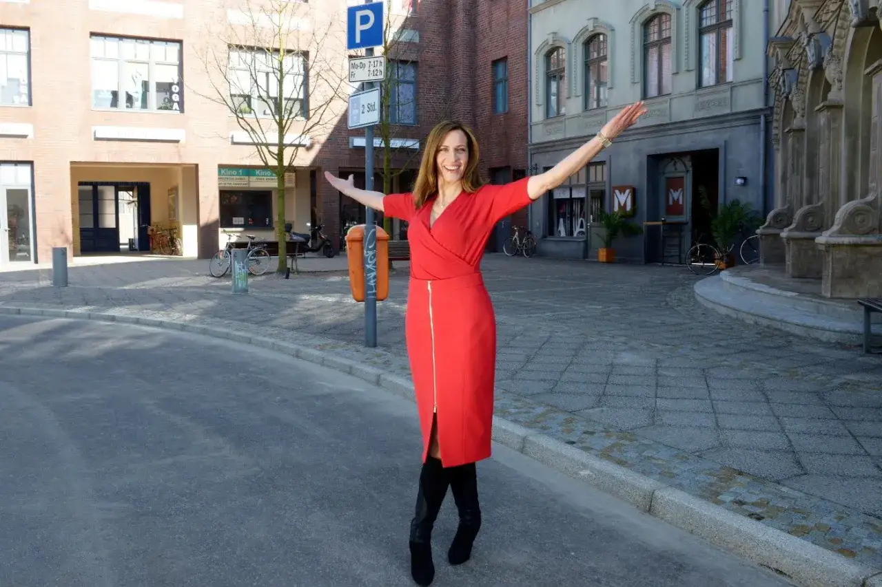 Frau in rotem Kleid mit ausgebreiteten Armen auf einer Straße, die an gute Zeiten schlechte Zeiten erinnert.