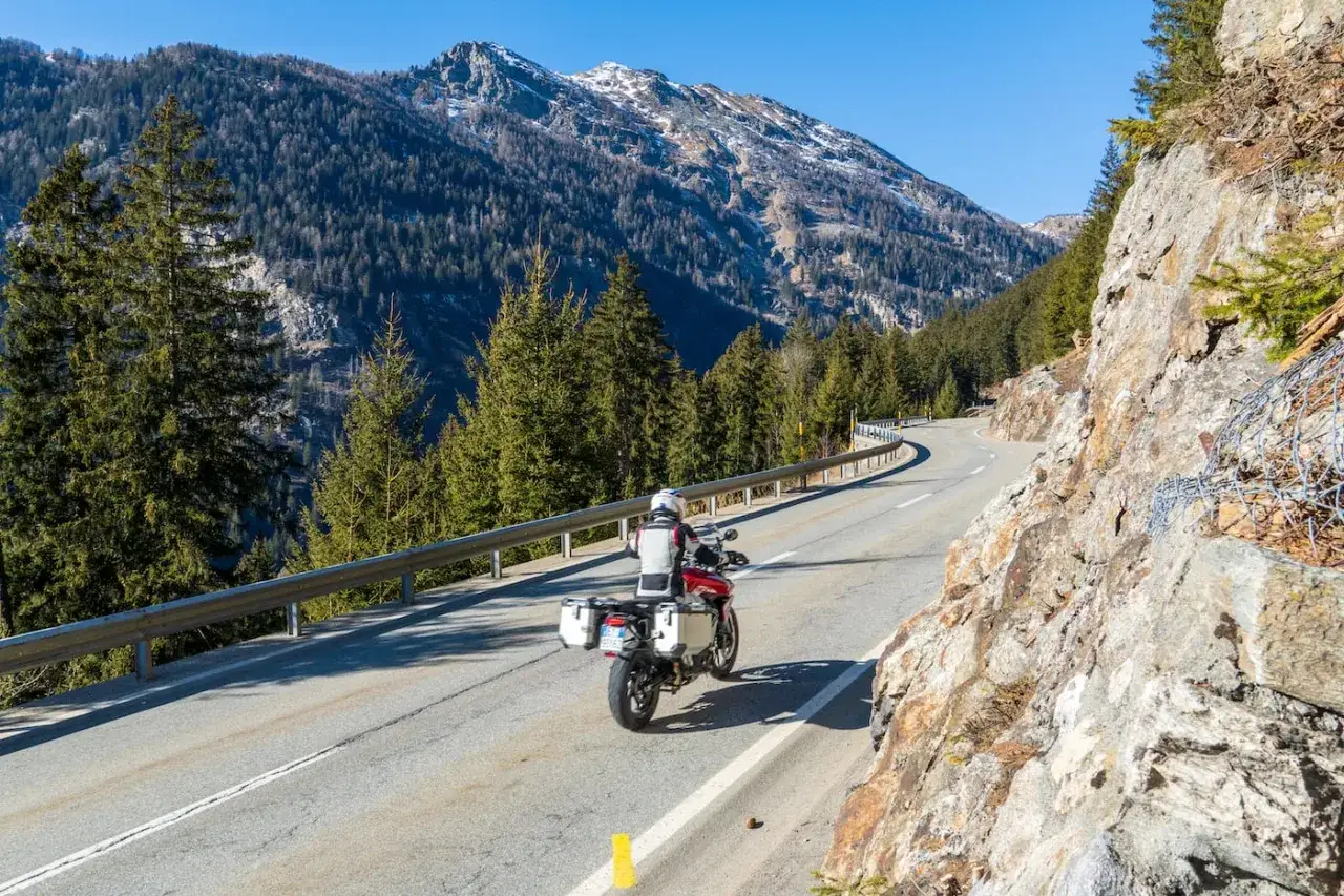 Motociclista affronta una curva su una strada di montagna, godendosi il panorama del passo della Novena.