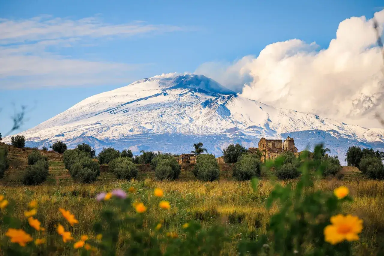 Wulkan Etna z ośnieżonym szczytem, kwitnące polne kwiaty i gaje oliwne. Taka jest pogoda na Sycylii w kwietniu.