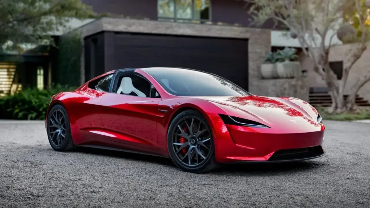 Lśniący czerwony Tesla Roadster 2 stoi przed nowoczesnym domem, gotowy do podr&oacute;ży.