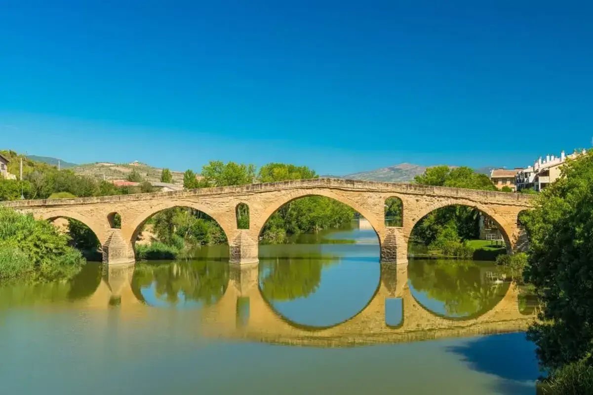 Puente medieval de piedra sobre un r&iacute;o tranquilo, reflej&aacute;ndose en el agua. Un paisaje id&iacute;lico para descubrir rutas cerca de Pamplona.