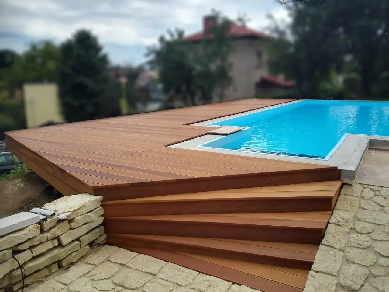 Nowy basen zabudowany deskami, z drewnianymi schodami prowadzącymi do wody.