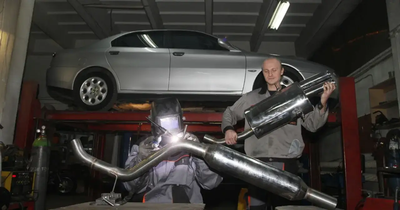 Mechanik spawa sportowy układ wydechowy dla srebrnego sedana na podnośniku.
