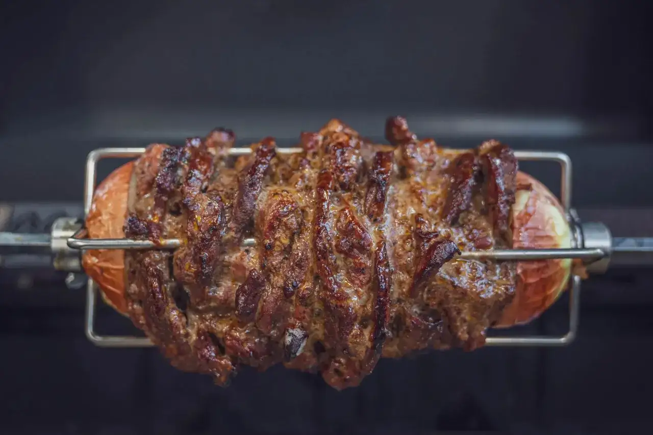 Saftiges Gyros vom Grill dreht sich auf einem Spieß, umgeben von einer großen Zwiebel.