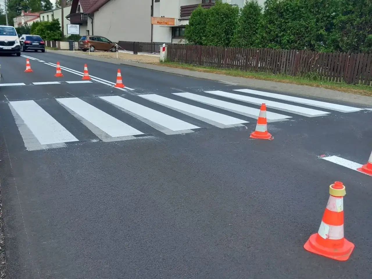 Świeżo malowane pasy na drodze jednojezdniowej dwukierunkowej. Pomarańczowe pachołki wyznaczają przejście dla pieszych.
