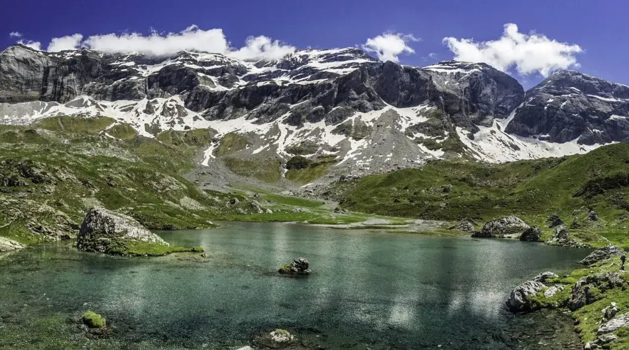 Le cirque de Troumouse, un lac d'altitude aux eaux turquoise, refl&egrave;te des montagnes majestueuses aux sommets enneig&eacute;s sous un ciel bleu &eacute;clatant.