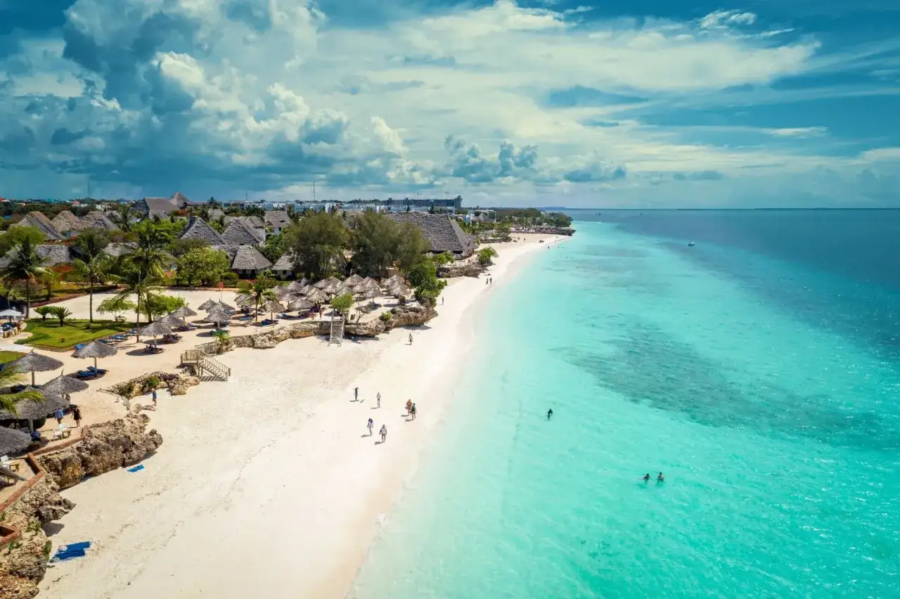 Rajska plaża na Zanzibarze na własną rękę. Turkusowa woda, biały piasek, palmy i urocze domki z krytymi dachami. Idealne miejsce na relaks.