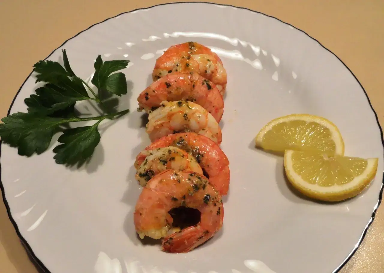 Deliziosi gamberoni in padella, conditi con erbe aromatiche e serviti con spicchi di limone fresco e un rametto di prezzemolo.