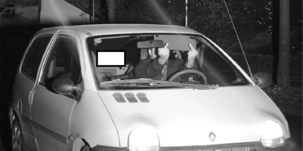 Blitzer Foto: Fahrer eines Kleinwagens zeigt den Mittelfinger, während er von einer Geschwindigkeitskamera erfasst wird.