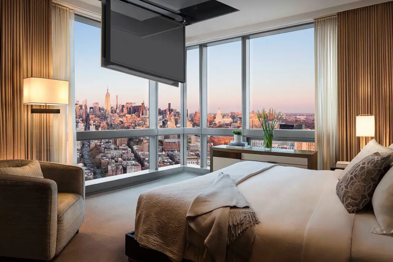 Camera da letto con vista su New York, dove una tv nascosta a soffitto scompare quando non in uso, lasciando spazio al panorama.