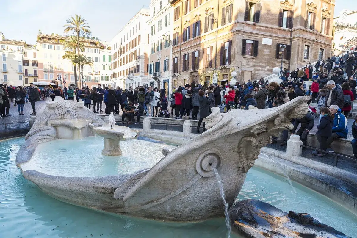 Fontaine de la Barcaccia à la Piazza di Spagna, Rome, avec une foule de touristes admirant le monument.