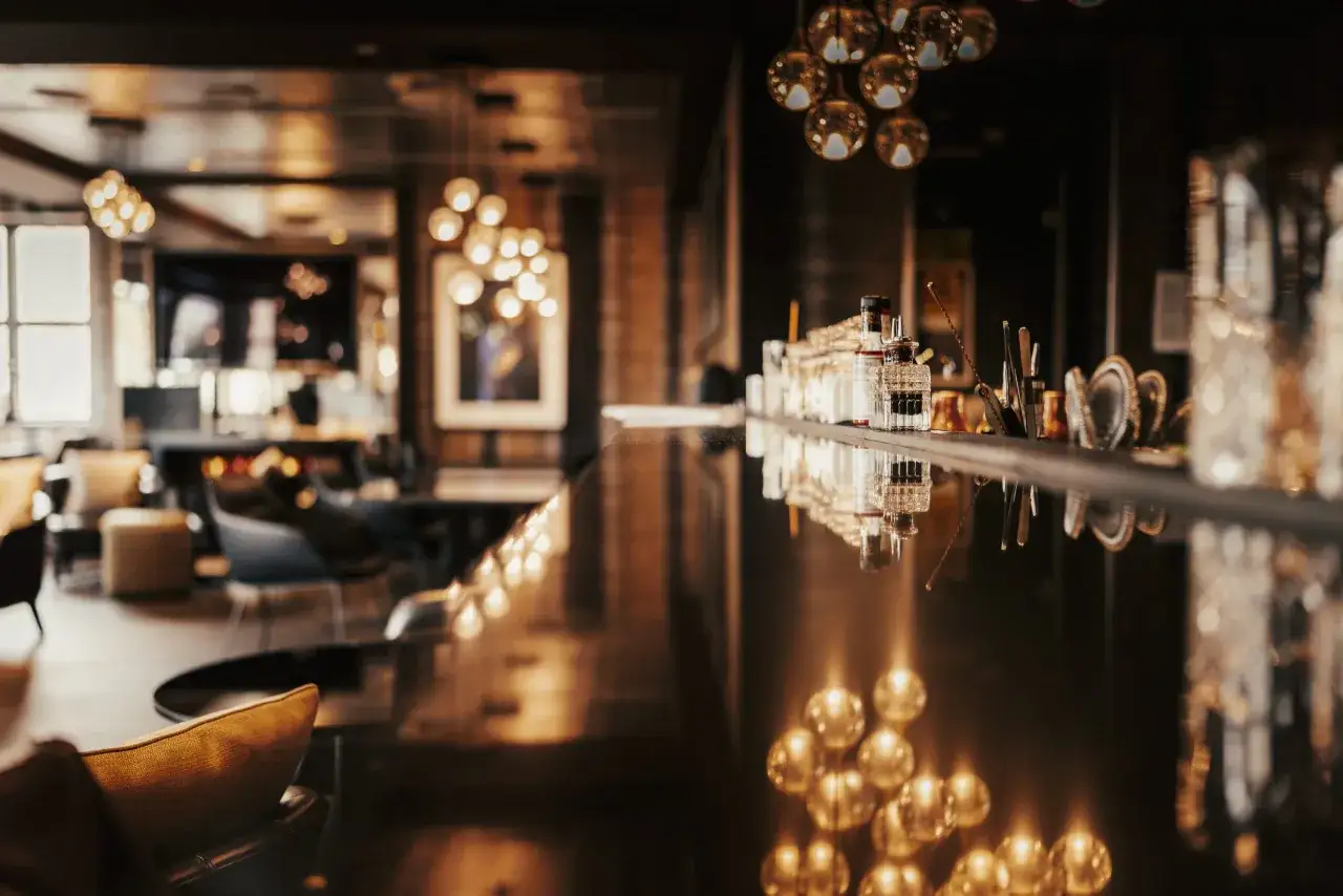 Ein stilvoller Bar-Bereich mit gedämpftem Licht und Spiegelungen. Flaschen und Gläser stehen bereit, vielleicht für einen **Oscar im Apropos**-Cocktail.