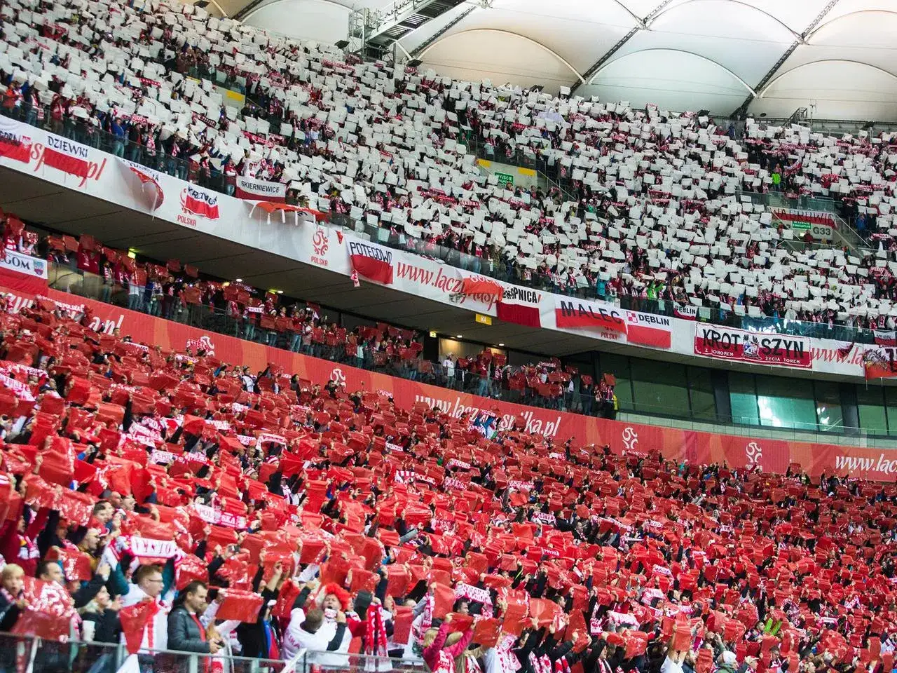 Tysiące kibiców na stadionie, tworzących biało-czerwone flagi i transparenty, wspierają swoje ulubione kluby piłkarskie.