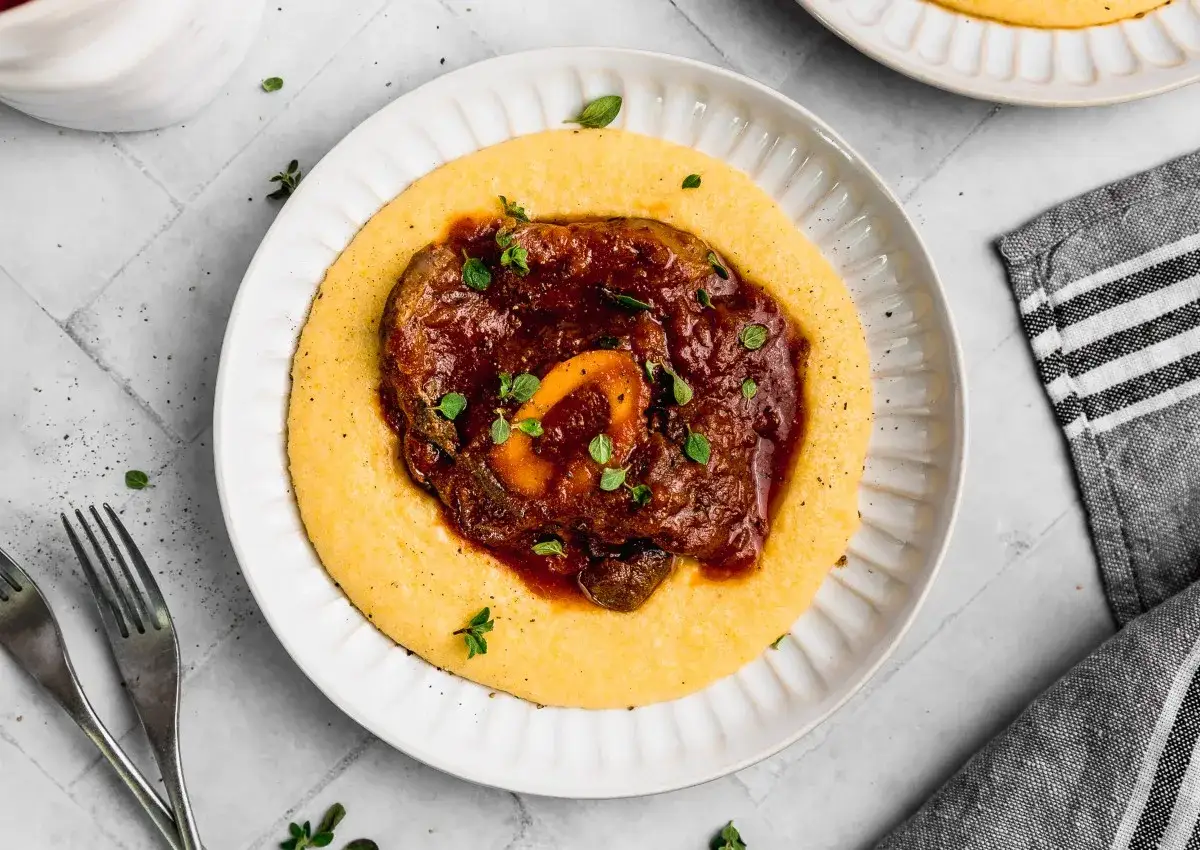 Un plato de polenta cremosa con un estofado de carne rico y sabroso, adornado con hierbas frescas.