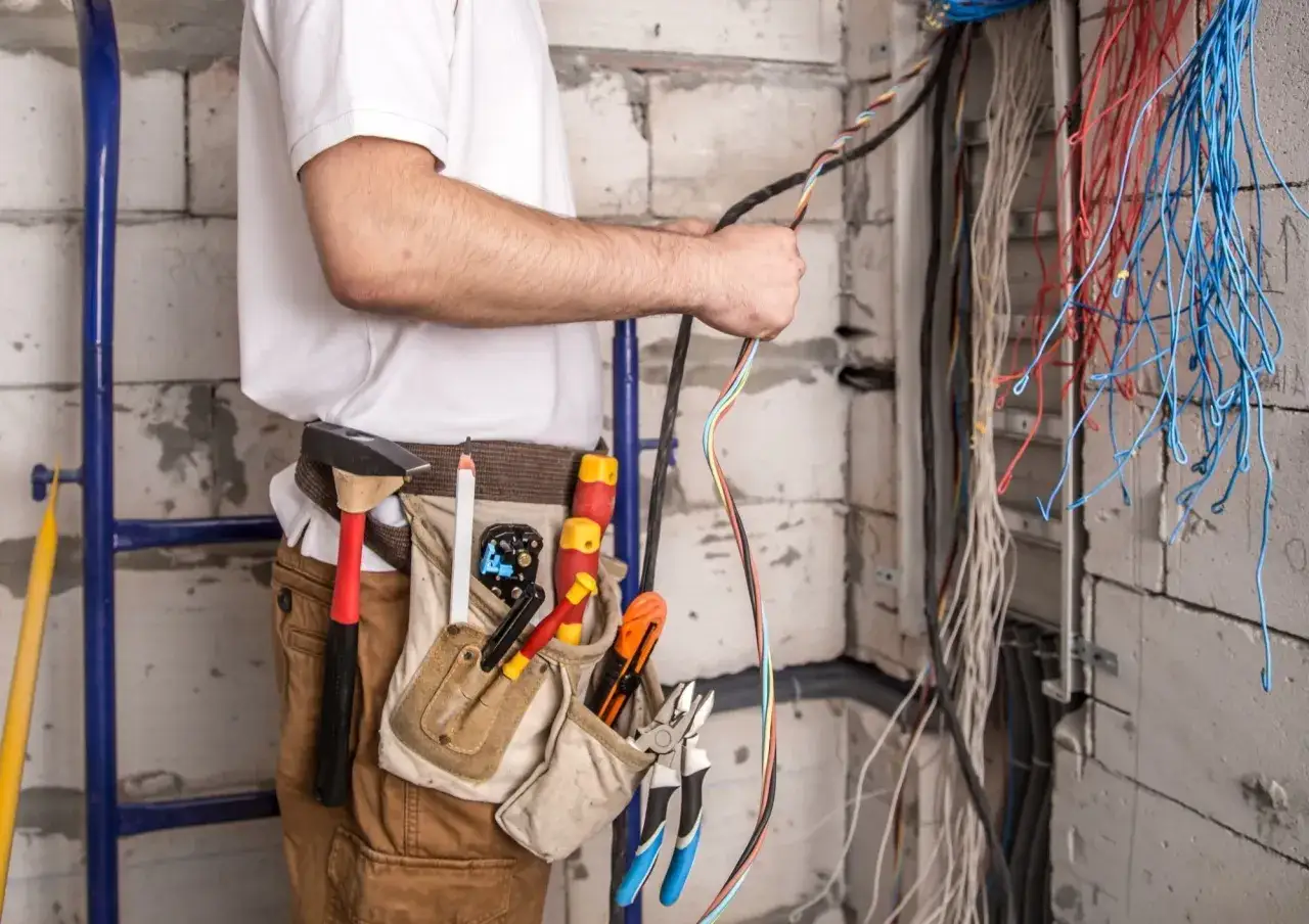 Un électricien manipule un type de câble électrique maison, entouré d'outils et de fils colorés prêts pour l'installation.