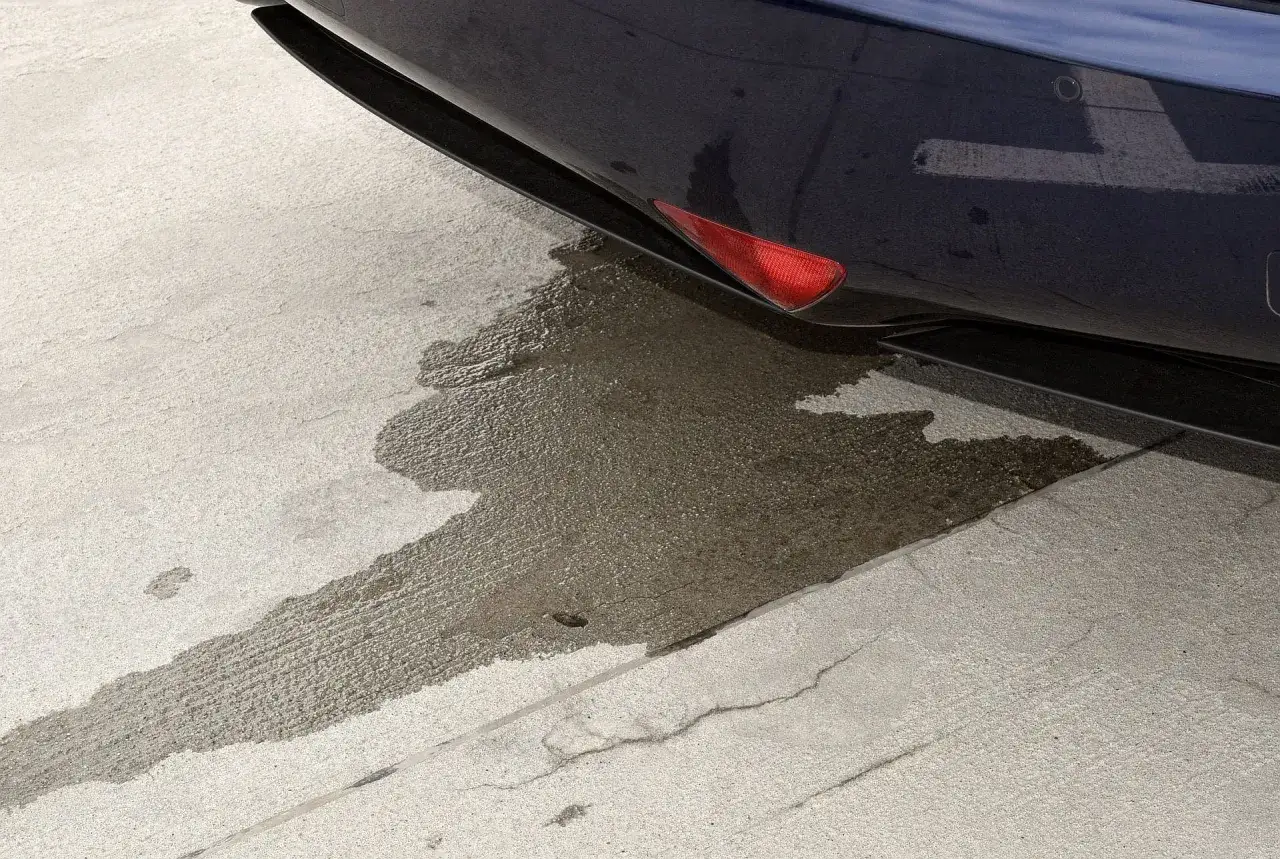 Auto pluje wodą z wydechu, tworząc mokrą plamę na betonowym podjeździe.