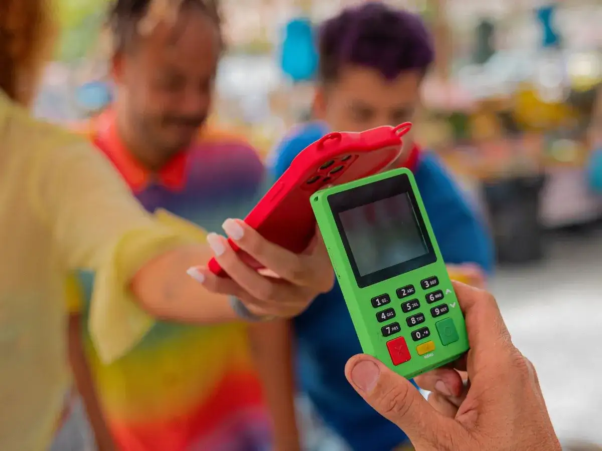 Płatność zbliżeniowa telefonem z kartą Revolut. Zielony terminal płatniczy i czerwone etui na telefon.