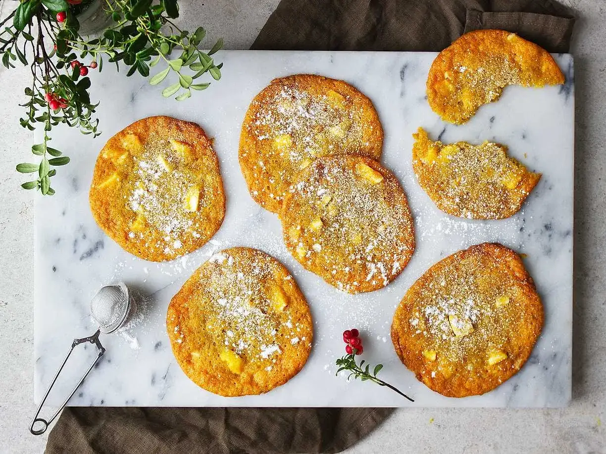 Saffranscookies med vit choklad, pudrade med florsocker, ligger på ett marmorfat. En bit är tagen från en cookie.