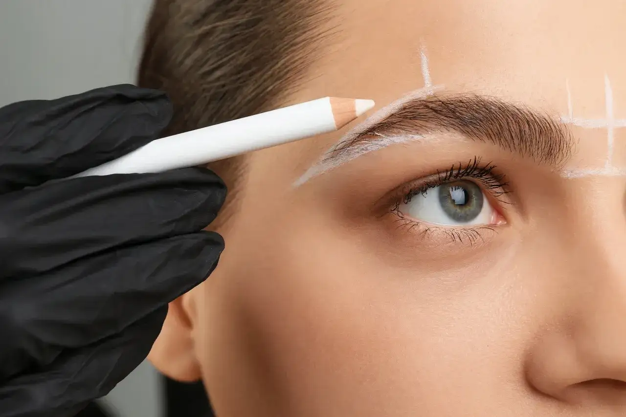 Une main gant&eacute;e de noir dessine la forme de sourcil test avec un crayon blanc.