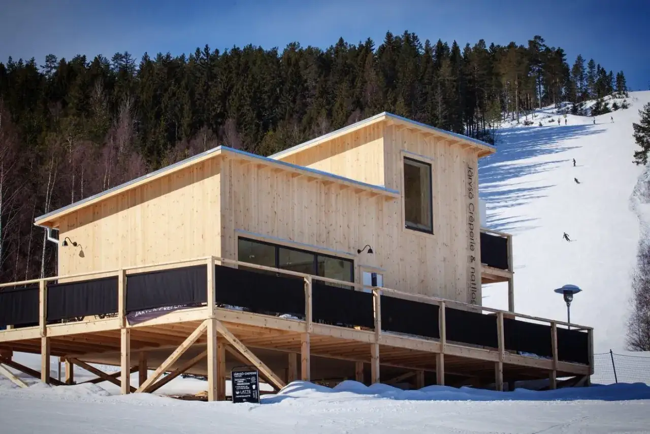Modernt b&b järvsö med träfasad vid skidbacke. Skidanläggning med skidåkare i bakgrunden.