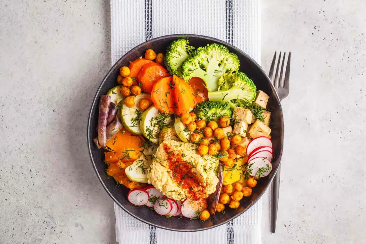 Un plato vibrante con hummus, br&oacute;coli, zanahoria, calabac&iacute;n, garbanzos y r&aacute;bano, perfecto para una dieta macrobi&oacute;tica equilibrada.