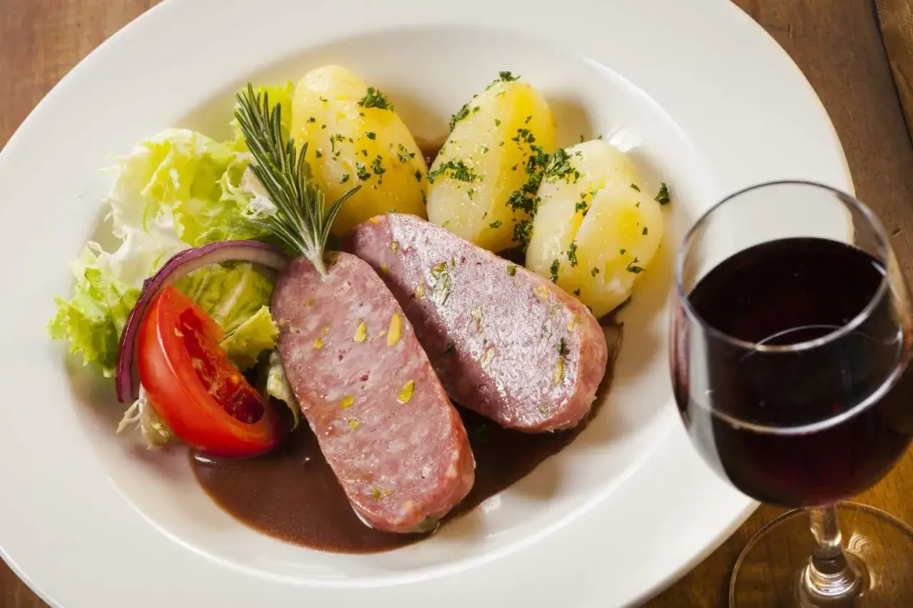 Saucisson lyonnais, pommes de terre et salade, un classique de la gastronomie lyonnaise, accompagné d'un verre de vin rouge.