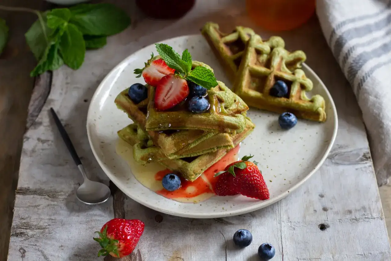 Grüne matcha waffeln gestapelt mit frischen Beeren und Minze, beträufelt mit Sirup. Ein Genuss für Augen und Gaumen.