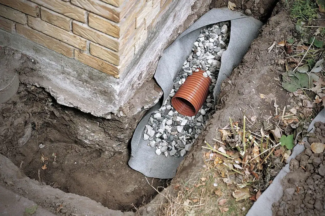 Drainagehaus: Ein Graben wird mit Vlies ausgelegt, gefüllt mit Kies und einem Drainagerohr, um das Fundament zu schützen.