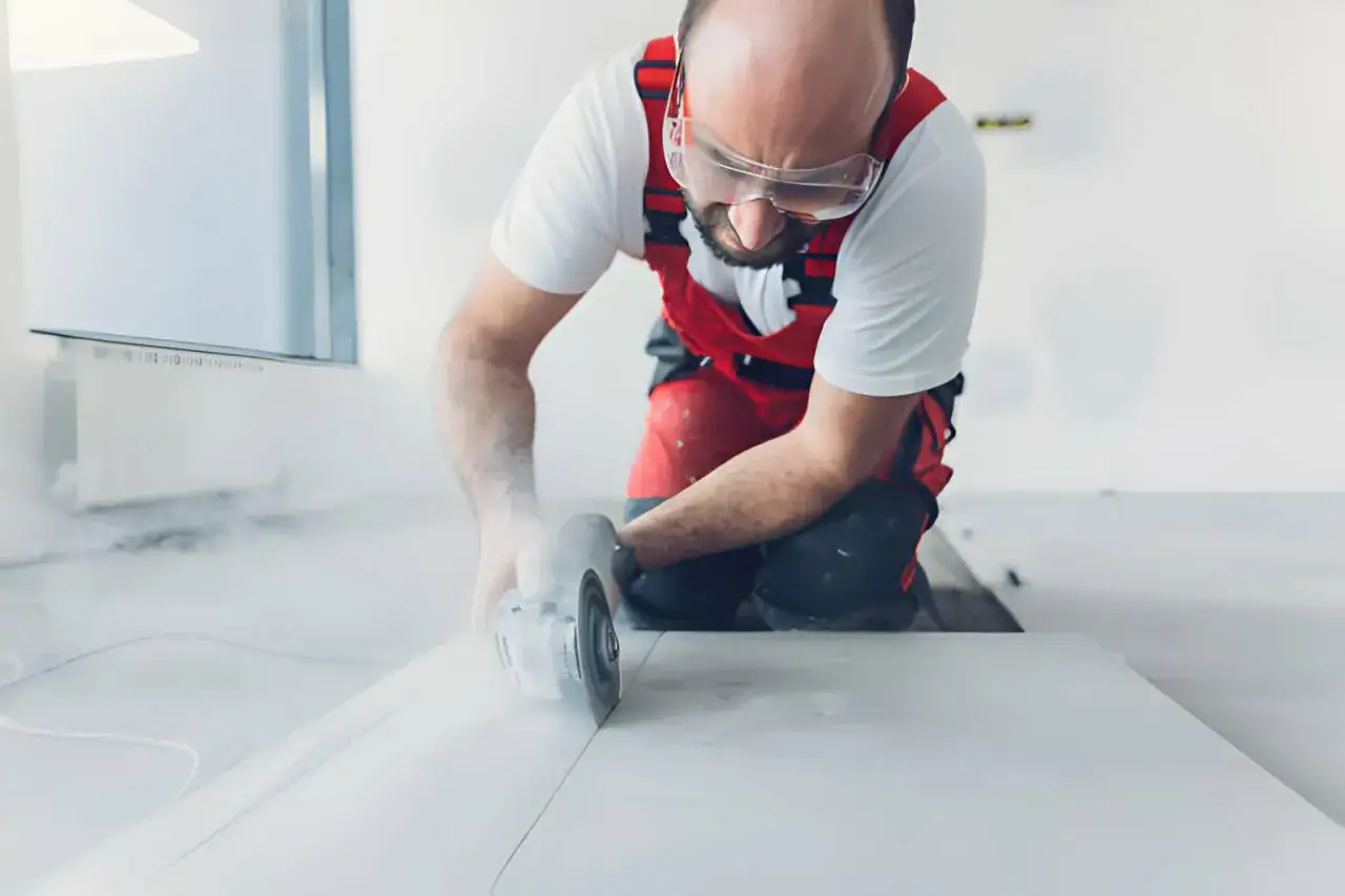 Operaio con occhiali protettivi taglia piastrelle senza tagliapiastrelle, creando polvere.