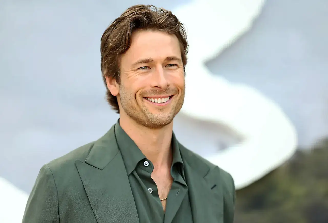 Glen Powell, bekannt aus Filmen wie Top Gun: Maverick, lächelt in einem grünen Anzug.