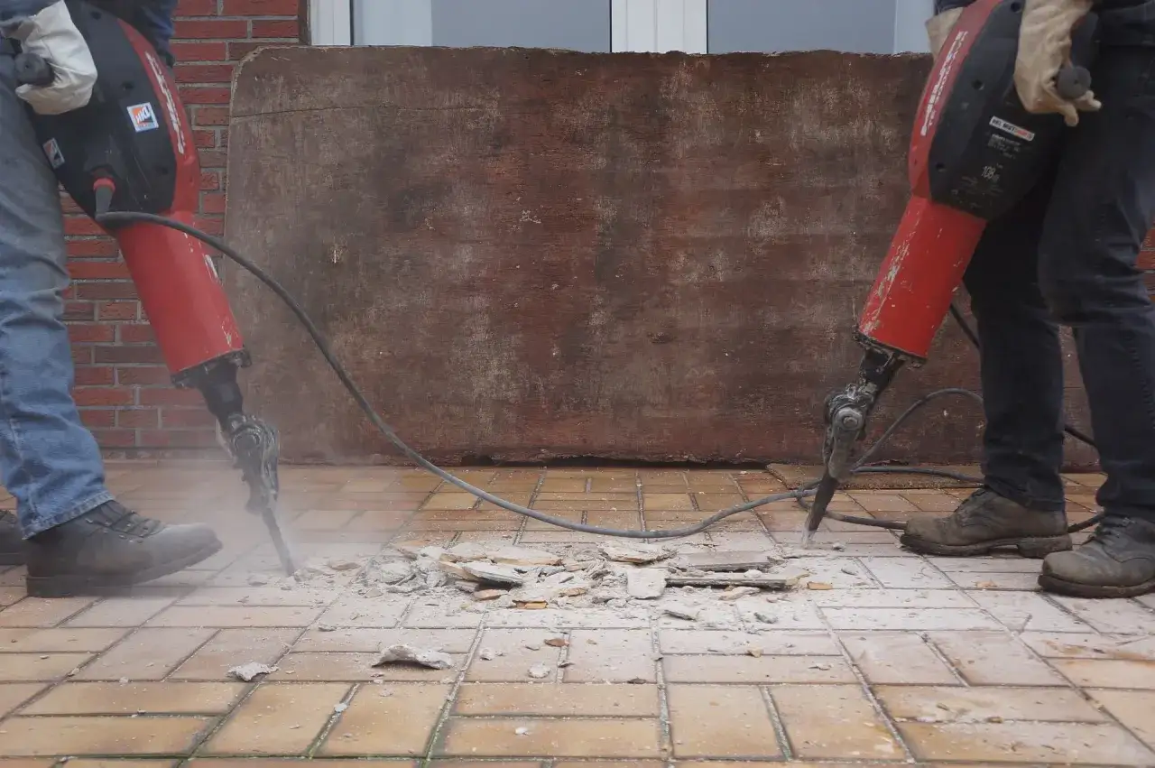 Dos personas realizan demolición manual de baldosas con martillos neumáticos.