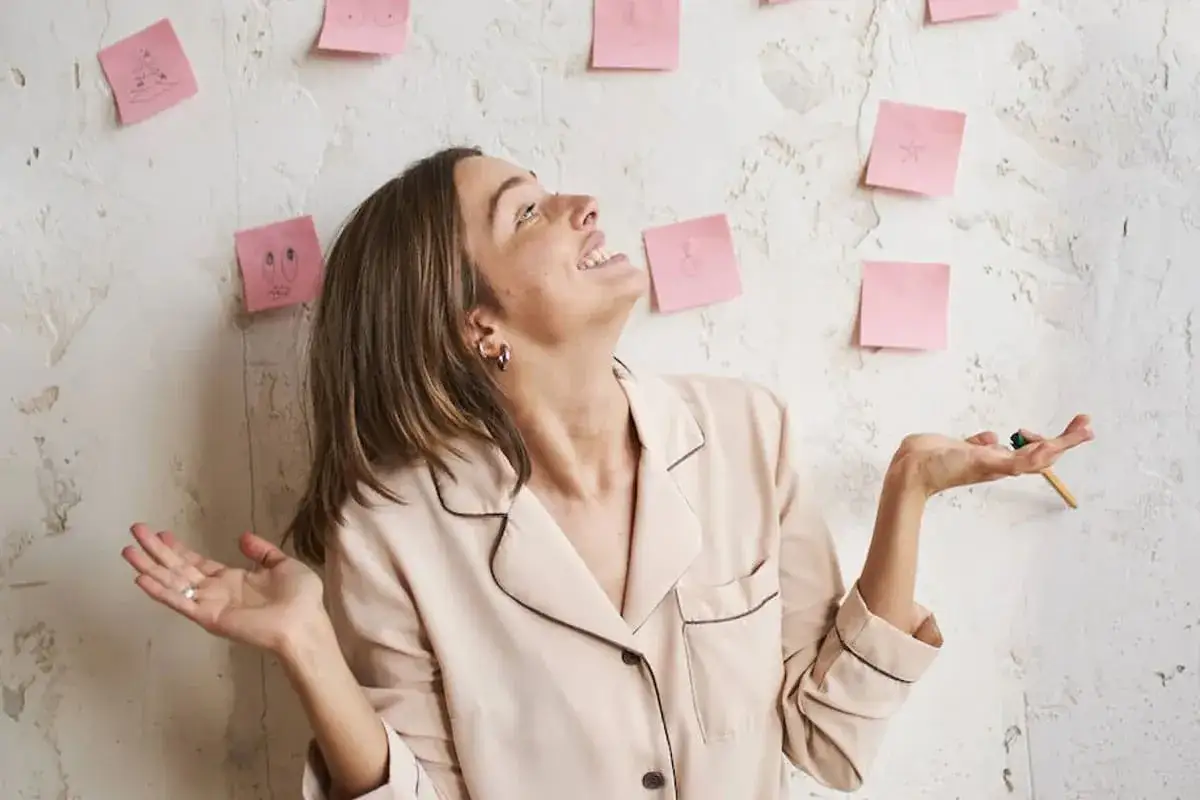 Mujer sonr&iacute;e mirando notas adhesivas con dibujos, planeando sus **objetivos en la vida**.