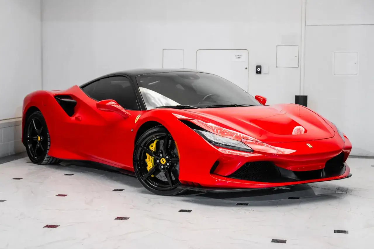 Czerwone Ferrari F8 Tributo z czarnym dachem i felgami, z żółtymi zaciskami hamulcowymi, lśni w garażu.
