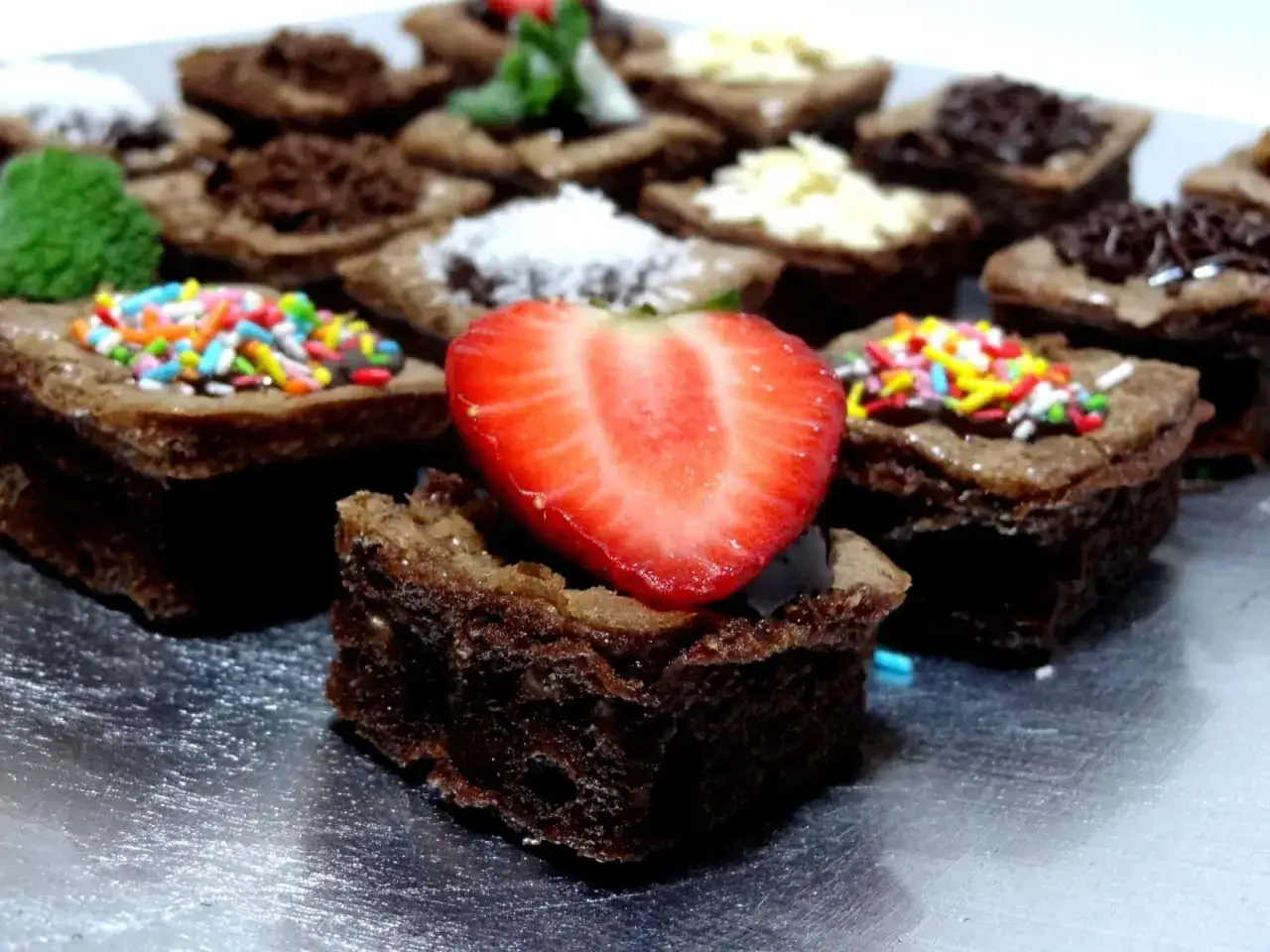 Deliciosos mini brownies con nueces, decorados con fresas, chispas de colores y coco rallado.