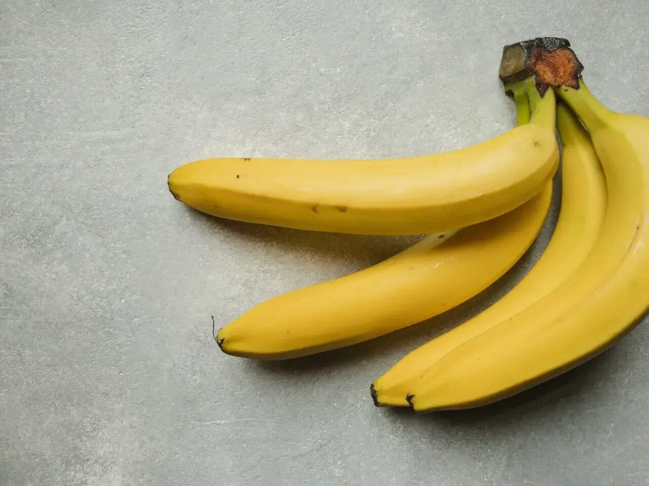 Kilka żółtych bananów na szarym tle. Zastanawiasz się, ile kalorii ma średni banan?
