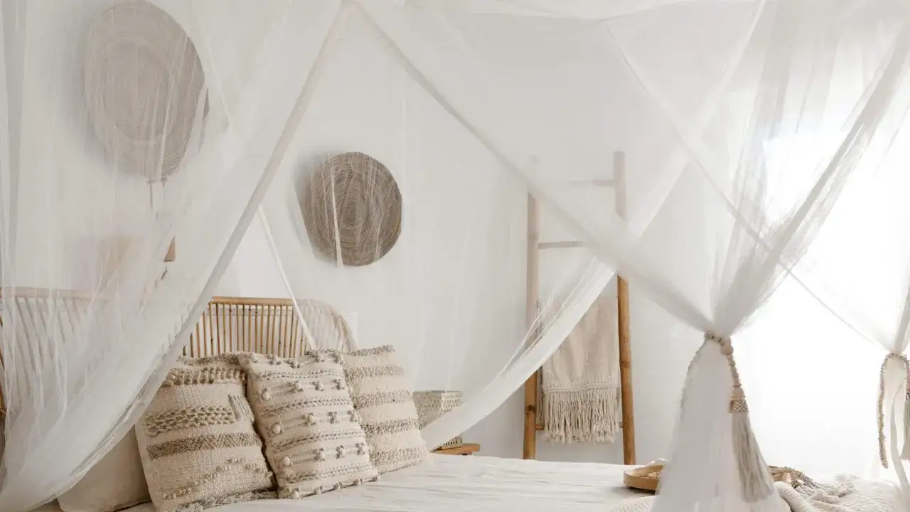 Lit douillet sous moustiquaire, une solution naturelle pour &eacute;loigner les moustiques la nuit. D&eacute;coration boh&egrave;me avec coussins textur&eacute;s et paniers en osier.